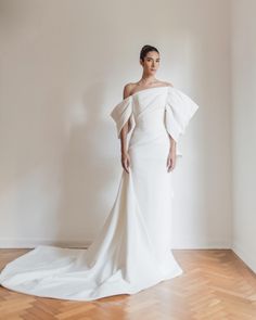 a woman in a white wedding dress standing on a wooden floor with her arms behind her back