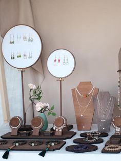 a table topped with lots of jewelry on top of wooden stand next to a vase filled with flowers