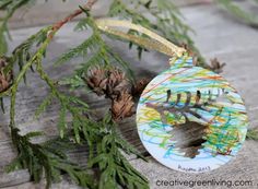 an ornament hanging from a tree branch with pine cones on the ground behind it