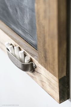 the chalkboard is attached to the wall by two metal clips that hold pens and pencils