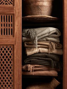 an open wooden cabinet filled with lots of folded blankets and blankets on top of each other