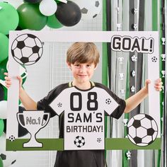 a young boy holding up a sign with soccer decorations around him and balloons in the background