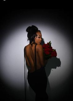 a woman in a black dress holding a bouquet of roses with her back to the camera