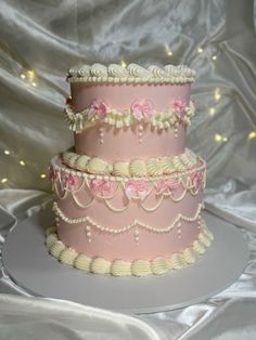 a three tiered cake with pink icing and white frosting decorations on top