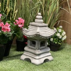 a small stone pagoda sitting on top of green grass next to potted plants and flowers