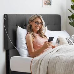 a woman sitting on a bed holding a cell phone and listening to music with headphones