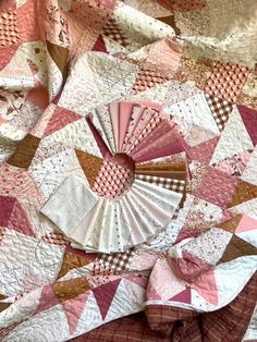 a pink and brown quilt on top of a bed with a fan in the middle