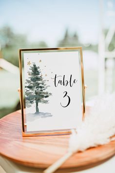 a table number with a pine tree painted on it and a white feather sitting next to it