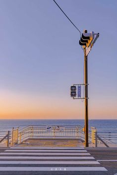 a street light sitting on the side of a road next to the ocean at sunset