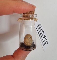 a hand holding a tiny glass jar with dirt inside and a small rock in it