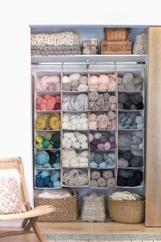 a shelf filled with lots of yarn next to a chair and basket on the floor