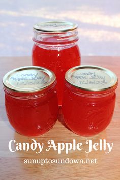 three jars filled with candy apple jelly sitting on top of a wooden table next to each other