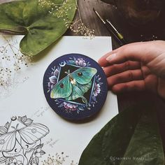 a person holding a paper with a butterfly on it next to some plants and flowers