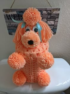 an orange stuffed animal sitting on top of a white toilet seat in a bathroom with a sign hanging above it