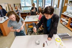 two students in a science lab looking at an object on a table while another student watches