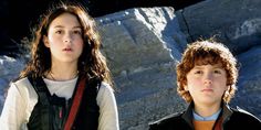 two young boys standing next to each other in front of some rocks and snow covered mountains