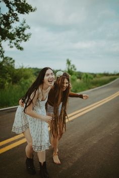 two young women are standing on the side of the road and laughing at each other