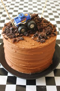 a birthday cake with chocolate frosting and monster trucks on top is sitting on a checkered tablecloth