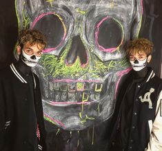 two young men standing next to each other in front of a chalkboard with a skull painted on it