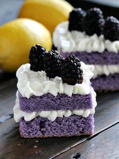 two purple desserts with white frosting and blackberries on top, sitting next to lemons