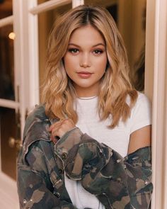 a beautiful young woman wearing camouflage clothing standing in front of an open door and looking at the camera