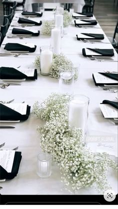 a long table is set with black and white place settings, silverware, and baby's breath flowers