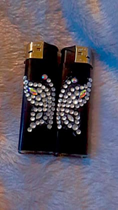 two black lighters with white and silver designs on them sitting on a fur surface