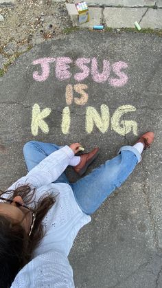 a woman laying on the ground with her feet up and writing jesus is king in chalk