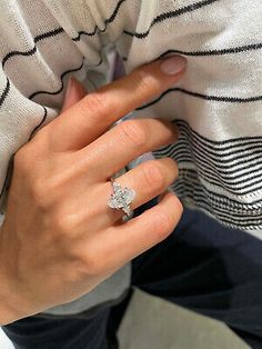 a woman's hand with a diamond ring on her finger, sitting in front of a white sweater