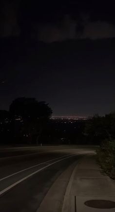 an empty street at night with the lights on and trees in the foreground behind it