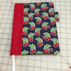 a notebook covered in cherries on a cutting board