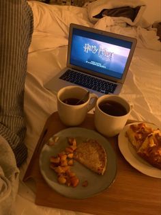 a laptop computer sitting on top of a bed next to two cups of coffee and food