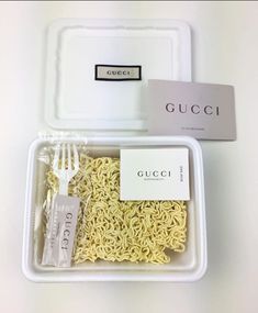 a plastic container filled with noodles next to a fork and box of gucci pasta