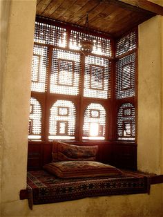 a bed sitting under a window next to a wooden frame with lots of windows on it