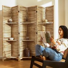 a woman sitting on a chair reading a book in front of a wooden wall unit