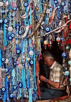 a man sitting in front of a display of beads and necklaces hanging from the ceiling