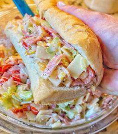 a hand holding a sandwich over a bowl of coleslaw