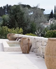 two large vases sitting on the side of a stone wall next to a fountain