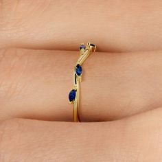 a woman's hand wearing a gold ring with blue stones on the side and an arrow shaped band