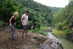 two people standing on the edge of a cliff overlooking a river