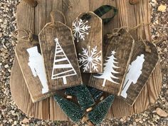 wooden tags decorated with christmas trees and snowflakes are on a wood board surrounded by pine cones