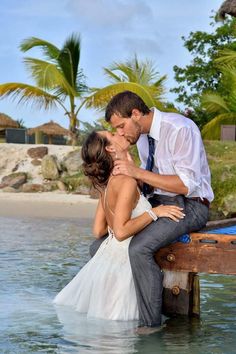 a man and woman are kissing in the water at their wedding ceremony on a dock