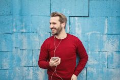 a man standing in front of a blue wall wearing headphones and listening to music