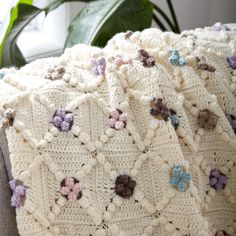 a white crocheted blanket sitting on top of a couch next to a potted plant