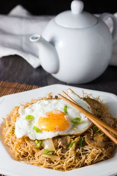 a white plate topped with noodles and an egg next to chopsticks on a wooden table