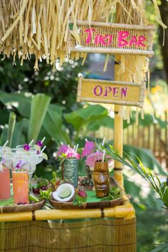 there is a table with drinks on it and straw umbrellas over the tables that have flowers in them