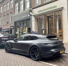 two porsches are parked on the street in front of a store with people walking by