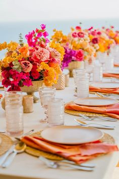 the table is set with orange, pink and yellow flowers in vases on each side