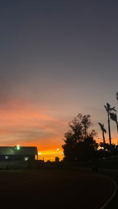 the sun is setting behind palm trees and a bus parked on the side of the road