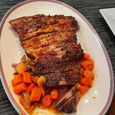 a white plate topped with meat and carrots on top of a wooden table next to a fork